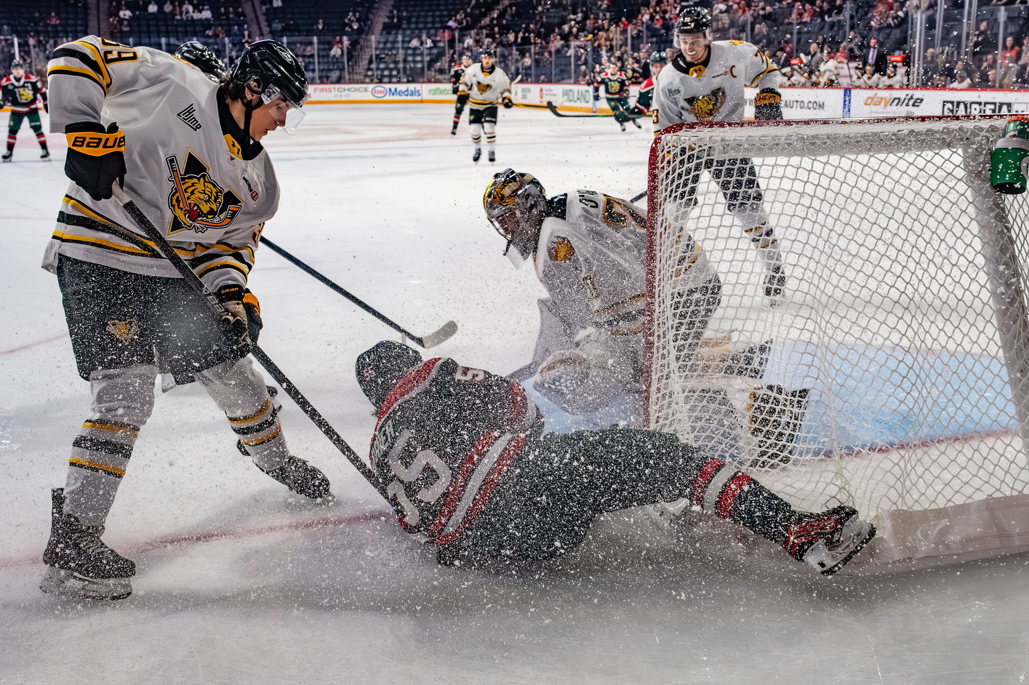 Halifax Mooseheads forward crashes into the crease and collides with the Victoriaville Tigres goalie at the side of the net, sending up a spray of ice as defenders converge.