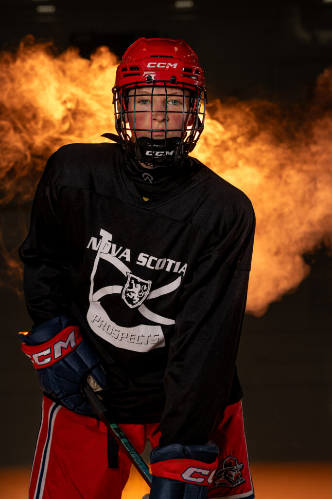 Youth hockey player posed with dramatic lighting and orange smoke during a custom sports portrait session in East Hants, Nova Scotia.